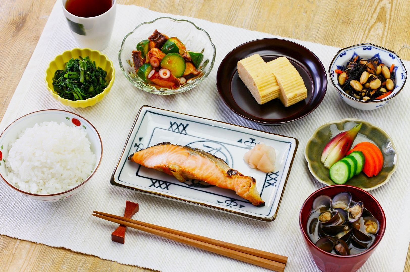 A Japanese meal set with grilled salmon, rice, tea, pickled vegetables, rolled omelette, assorted vegetables, seaweed salad, and miso soup.