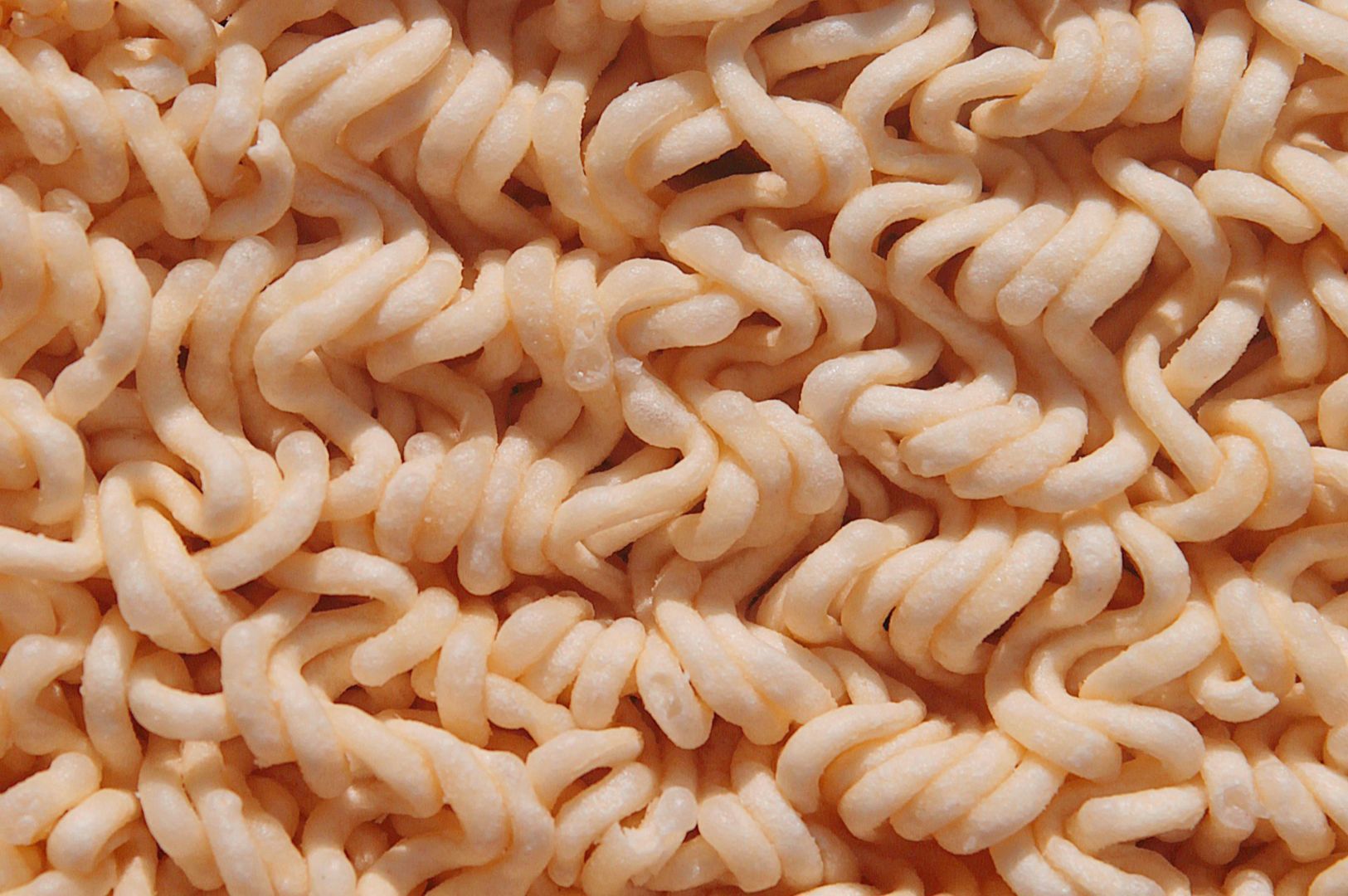 Close-up of dry, wavy instant noodles, tightly packed with a pale yellow hue, creating a textured and intricate pattern.