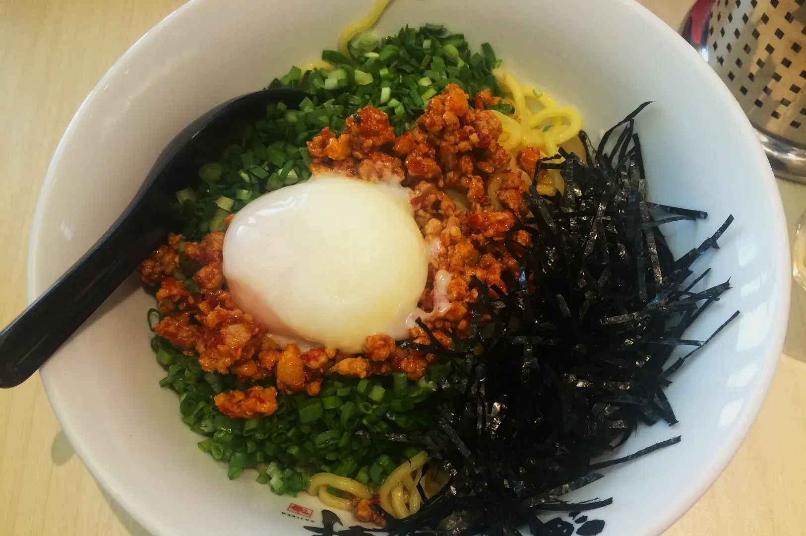 A bowl of ramen topped with minced meat, green onions, a soft-boiled egg, and shredded seaweed, creating a colorful and appetizing dish.