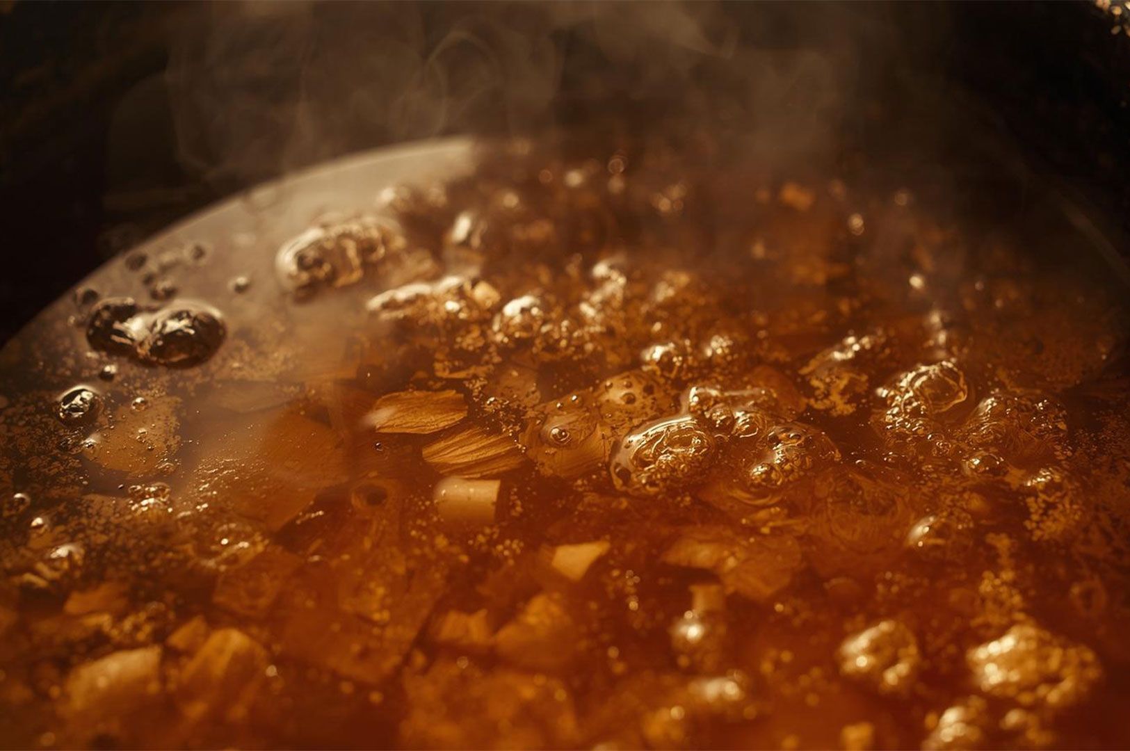 Extreme close-up of rich, amber-colored ramen broth vigorously boiling in a pot, showing bubbles and pieces of meat or bone simmering.