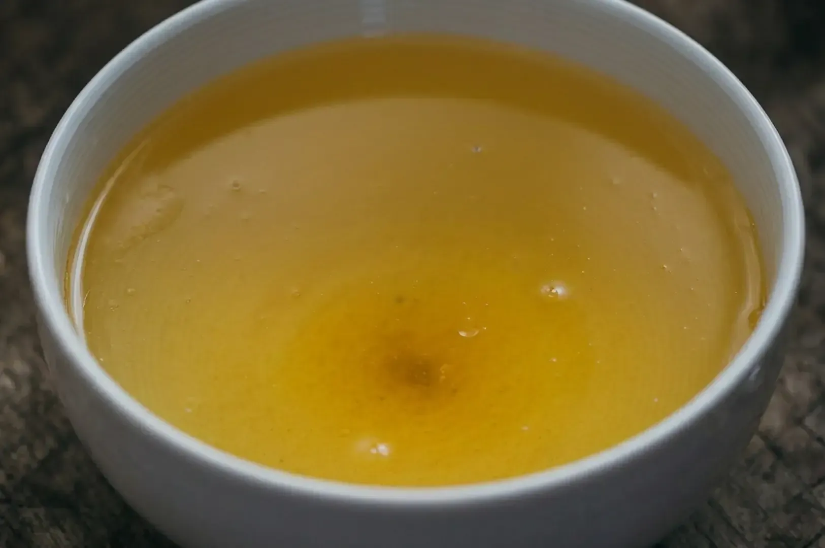 Crystal clear golden chicken broth in white bowl showing translucent clarity.
