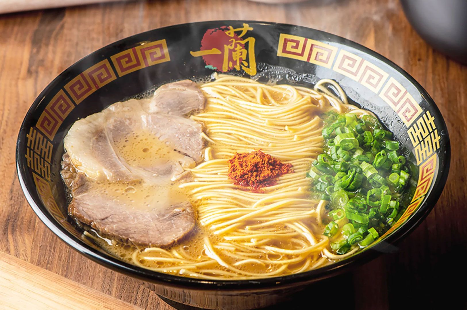 Close-up of a classic Ichiran-style ramen bowl with thin noodles, savory broth, two slices of chashu, finely chopped spring onions, and a sprinkle of red chili powder.