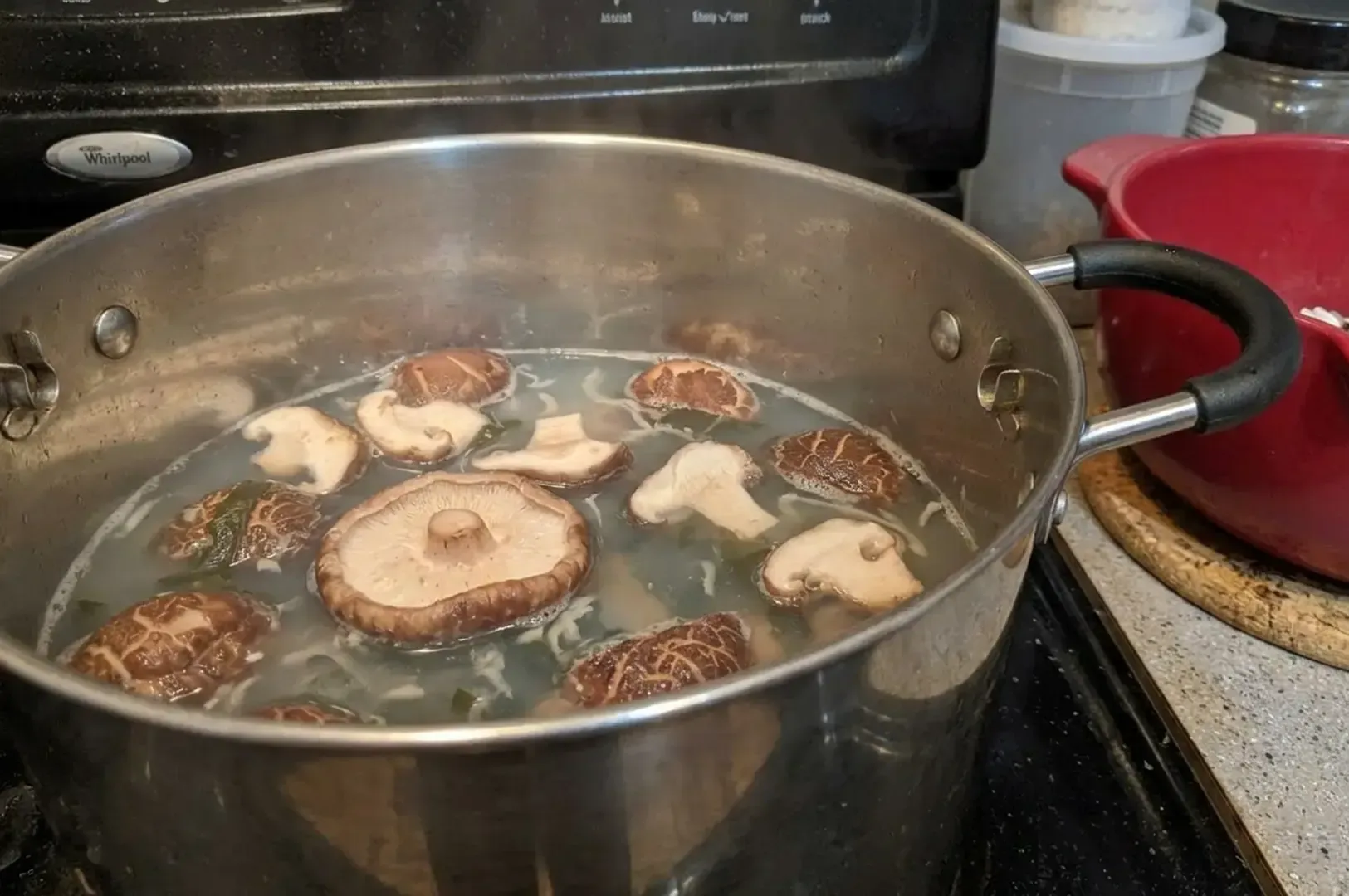 Shiitake mushrooms simmering in dashi broth in a stainless steel pot.