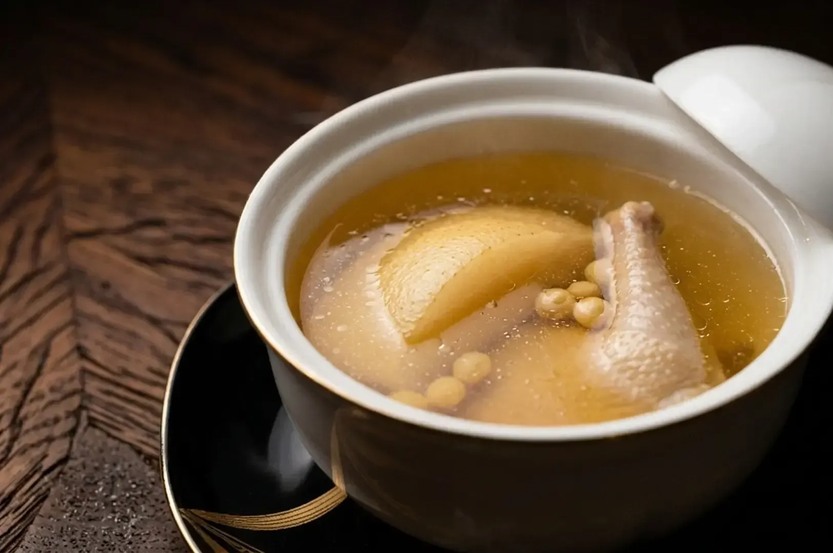 Clear golden chicken broth with chicken pieces and aromatics in white ceramic bowl.