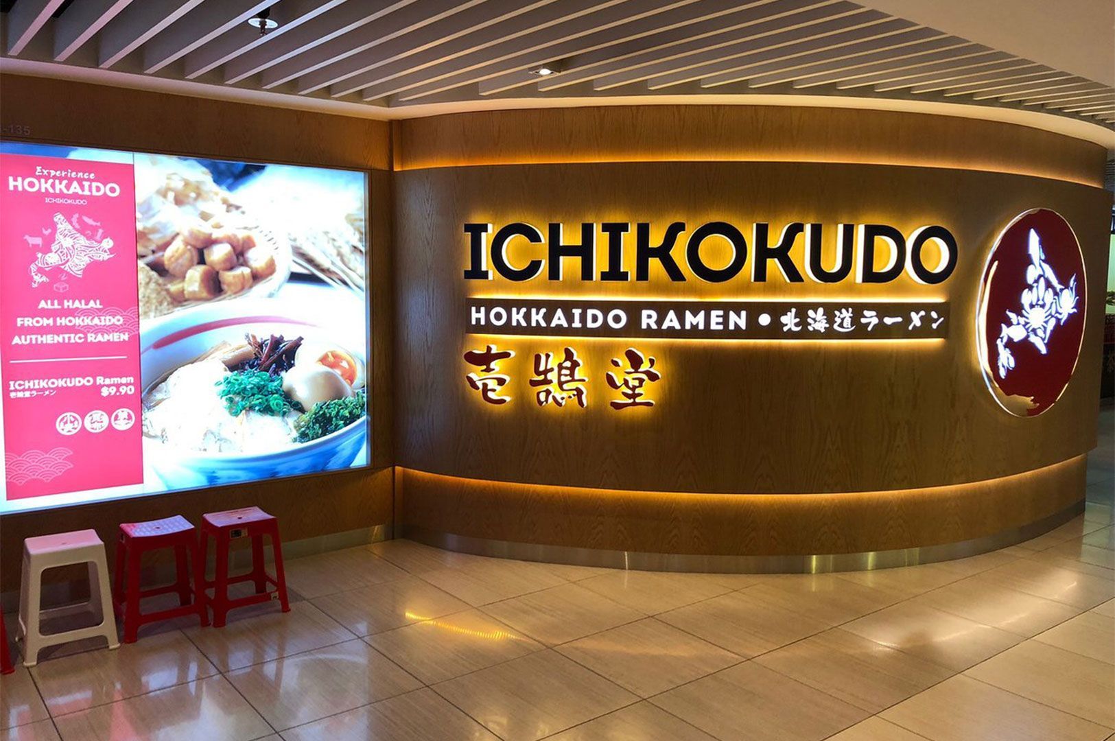 The brightly lit wooden facade of Ichikokudo Hokkaido Ramen. The signage is in large English and Japanese characters and prominently features a note: