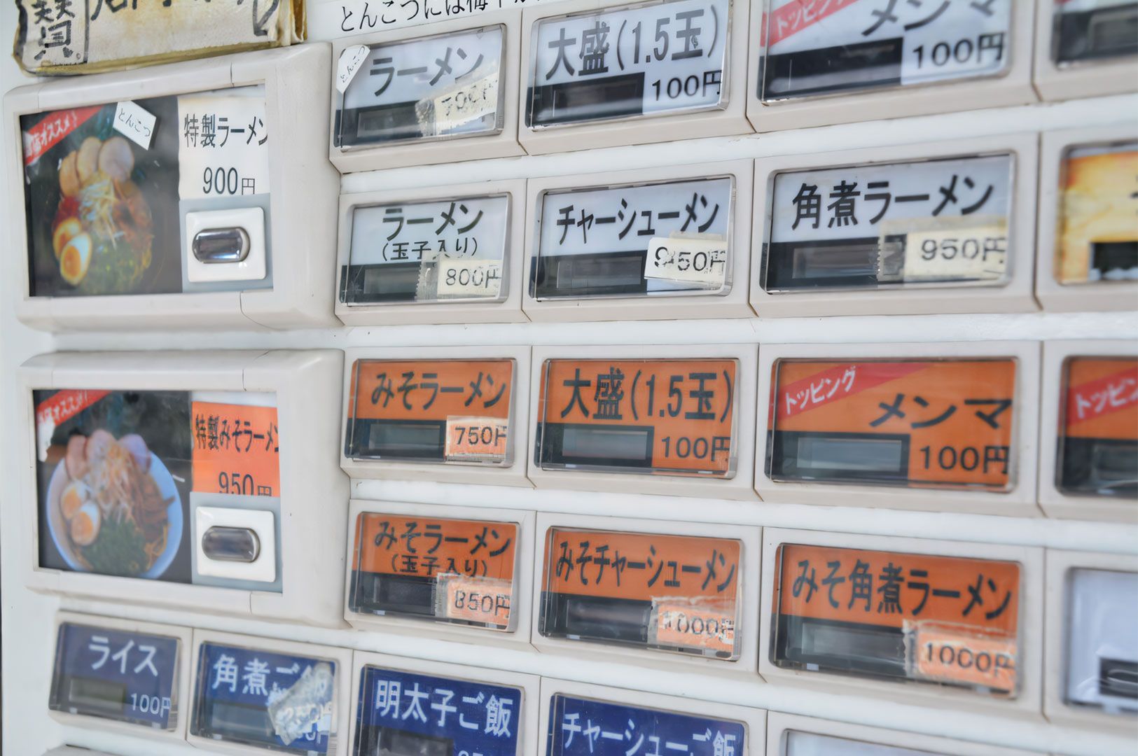 A close-up of a Japanese ticket vending machine (kenbaiki) displaying various ramen options and prices in yen, including Miso Ramen, Chashu, and Kaedama (extra noodles).