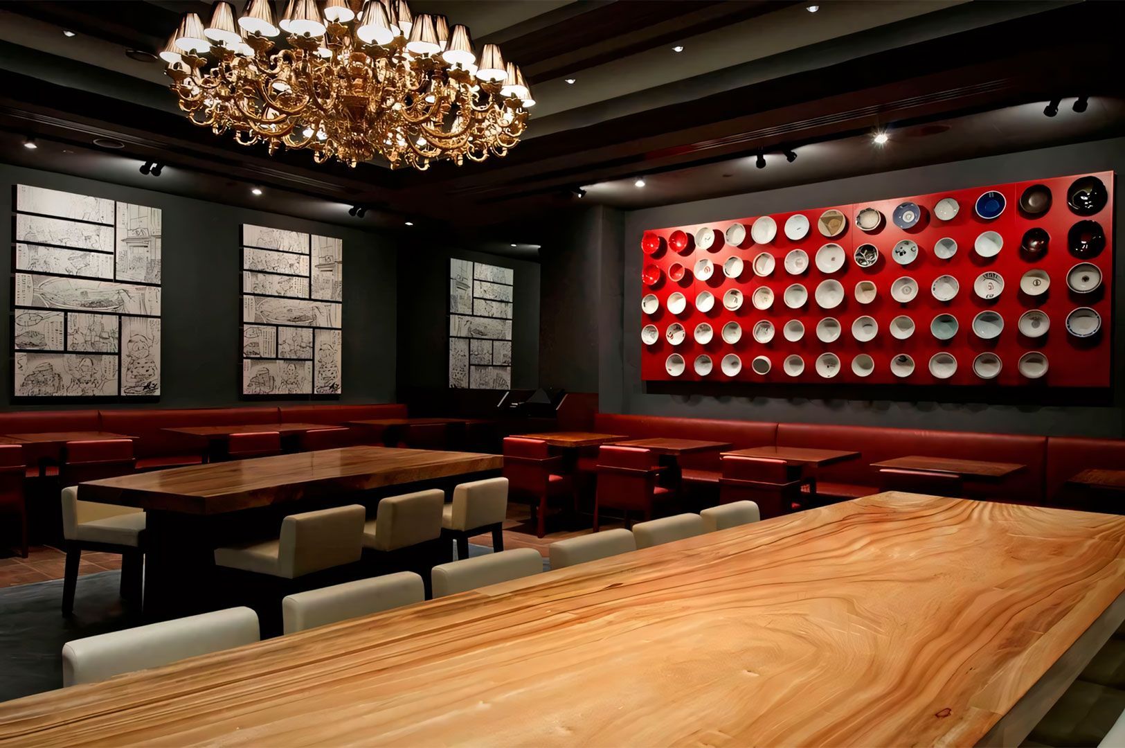 Upscale modern Japanese restaurant interior with large wooden communal tables, red leather seating, a gold chandelier, and a wall display of decorative plates.