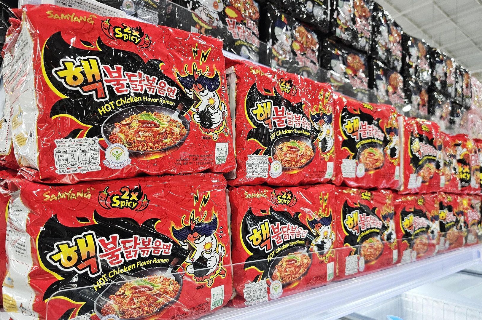 Retail shelf stacked high with bright red packages of Samyang 2x Spicy Hot Chicken Flavor Ramen (Buldak Bokkeum Myeon).