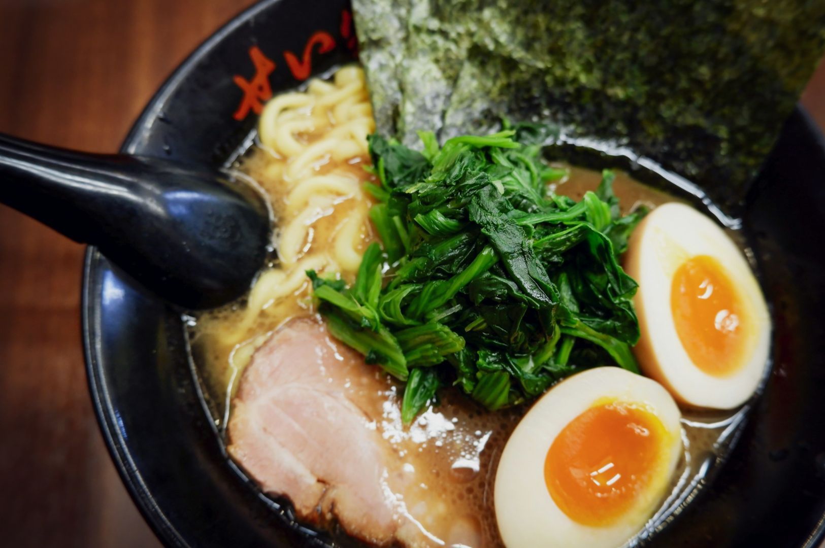 A steaming bowl of ramen features sliced pork, soft-boiled eggs with jammy yolks, spinach, seaweed, and noodles in rich broth, evoking warmth and comfort.
