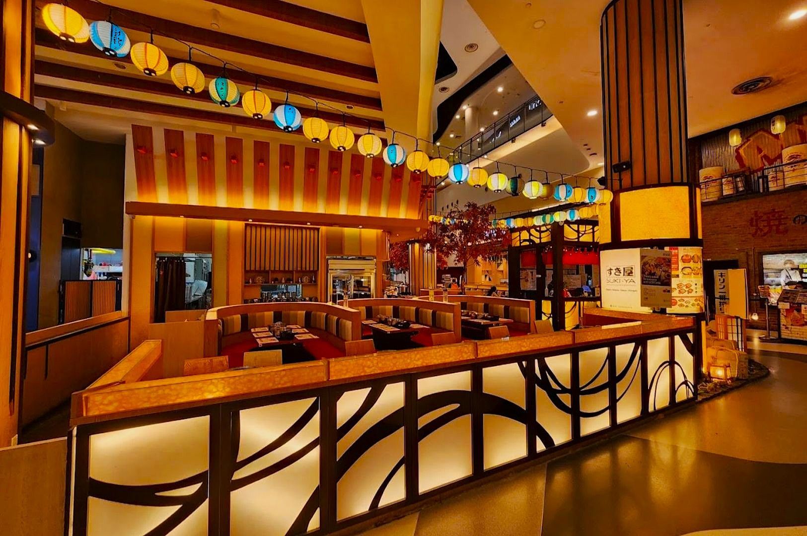 Modern, warmly lit Japanese restaurant interior with curved booths, wooden decor, and colorful hanging lanterns, creating a cozy and inviting atmosphere.