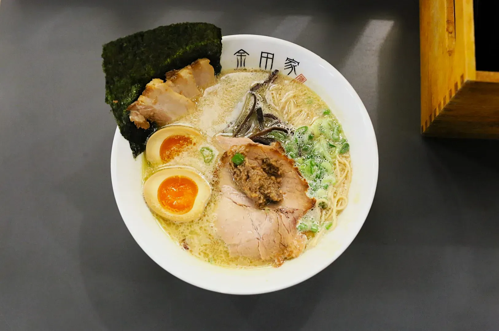 A bowl of ramen with sliced pork, soft-boiled eggs, seaweed, mushrooms, and scallions in a creamy broth, creating a rich and appetizing appearance.