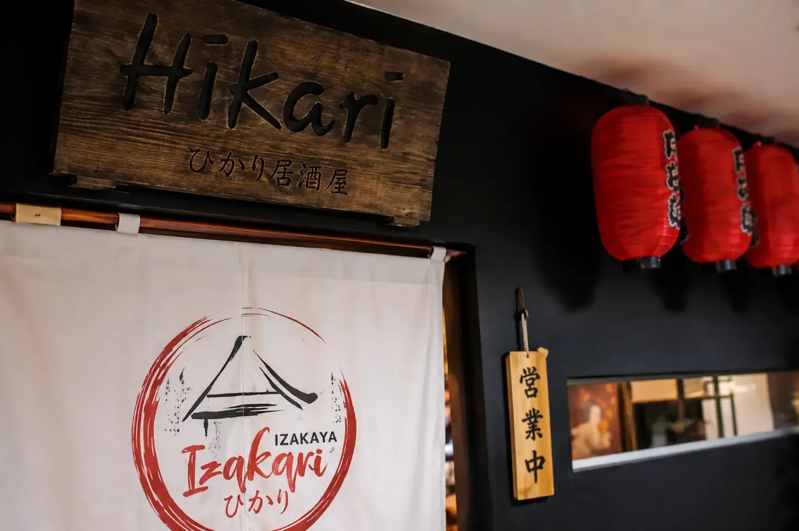 Hikari Izakaya wooden signboard with red Japanese lanterns and traditional noren curtain at entrance