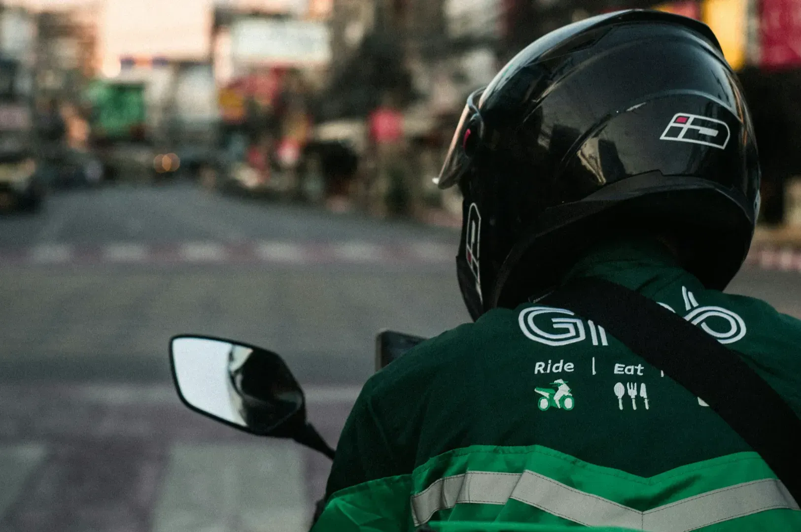 Delivery driver on a scooter at dawn, wearing a green jacket with a helmet, rides through a quiet city street, creating a sense of early morning calm.