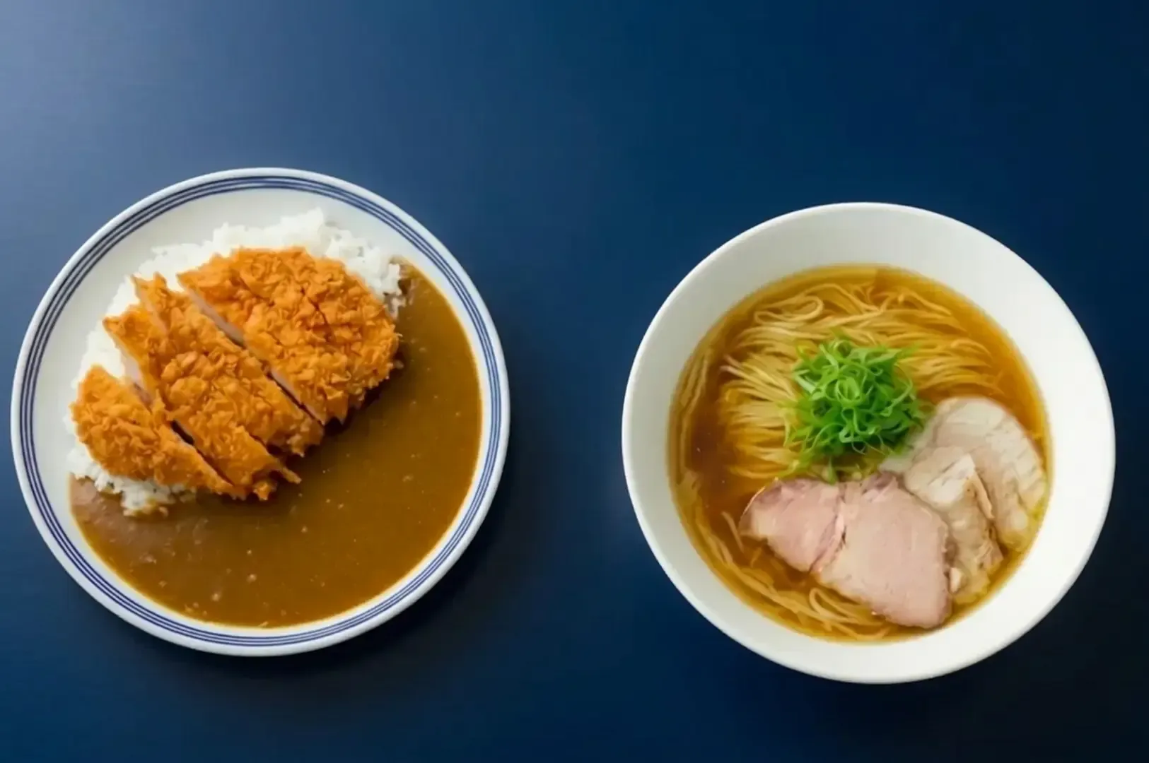 Plate of chicken katsu curry rice and a bowl of ramen with pork slices on a dark blue table