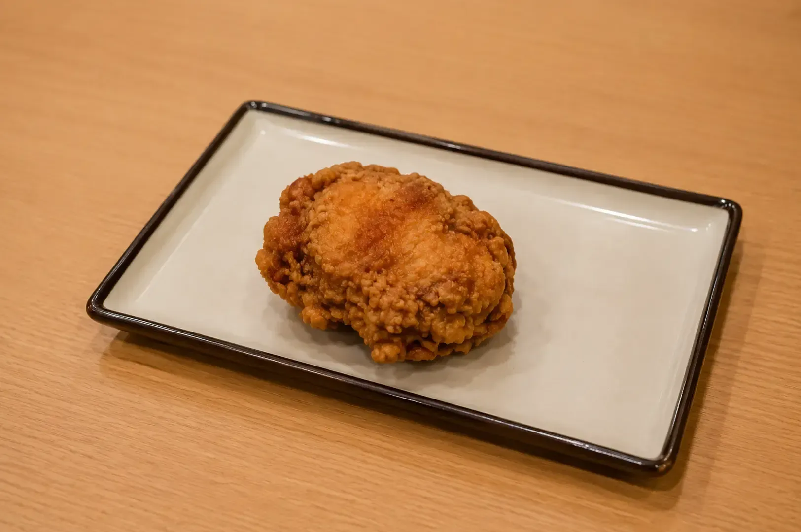 A piece of crispy Japanese fried chicken served on a rectangular white plate with a dark rim