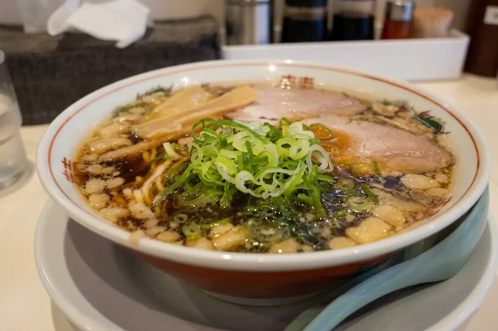 Onomichi ramen bowl with chashu pork, bamboo shoots, green onions, and pork fat in clear soy sauce broth.