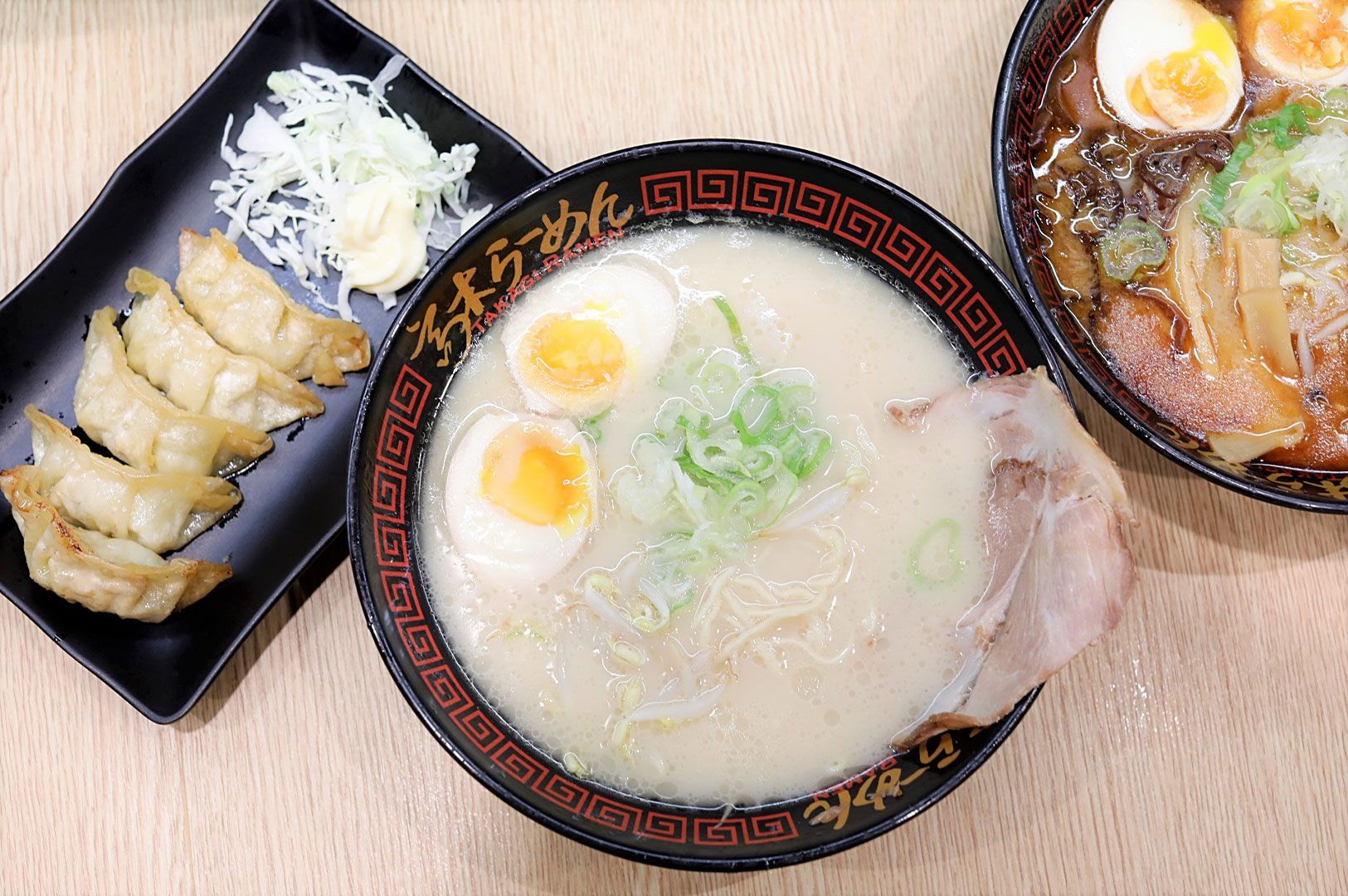 Overhead view of a creamy tonkotsu ramen bowl with chashu and eggs, served alongside a plate of pan-fried gyoza dumplings.