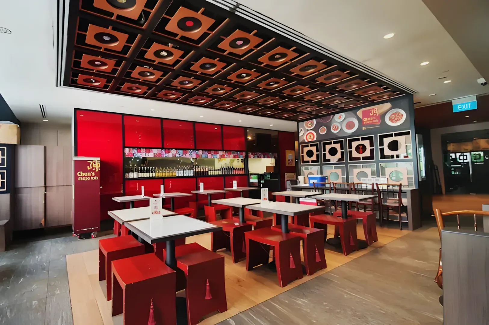 Spacious modern restaurant with red and black decor. Square tables are set with red stools. Walls feature vibrant images; ceiling has geometric patterns.