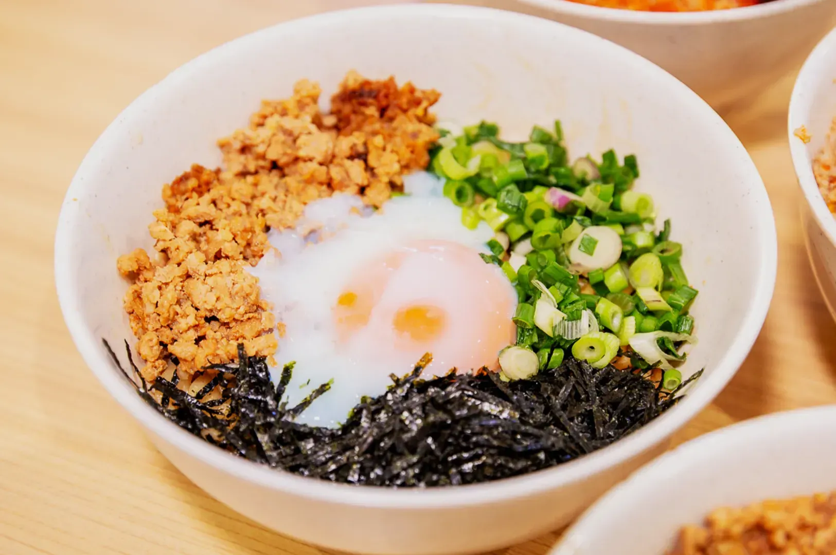 A bowl of ramen with minced meat, chopped green onions, shredded seaweed, and a soft-boiled egg on top, creating a colorful and appetizing dish.