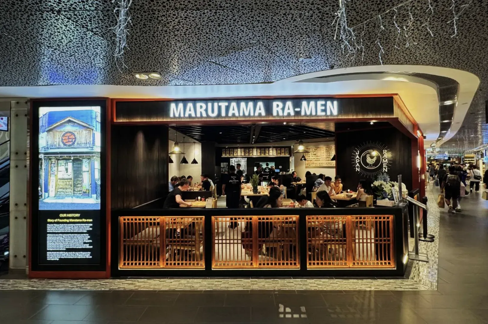 Bustling ramen restaurant with warm, inviting decor. Patrons enjoy meals inside, beneath a glowing 