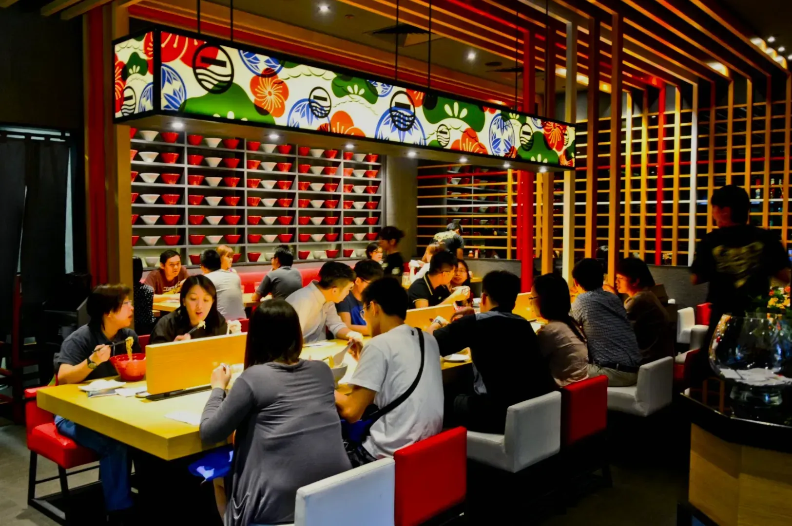 People enjoying a meal in a vibrant, modern restaurant with colorful wall art and geometric wooden decor, creating a warm, lively atmosphere.