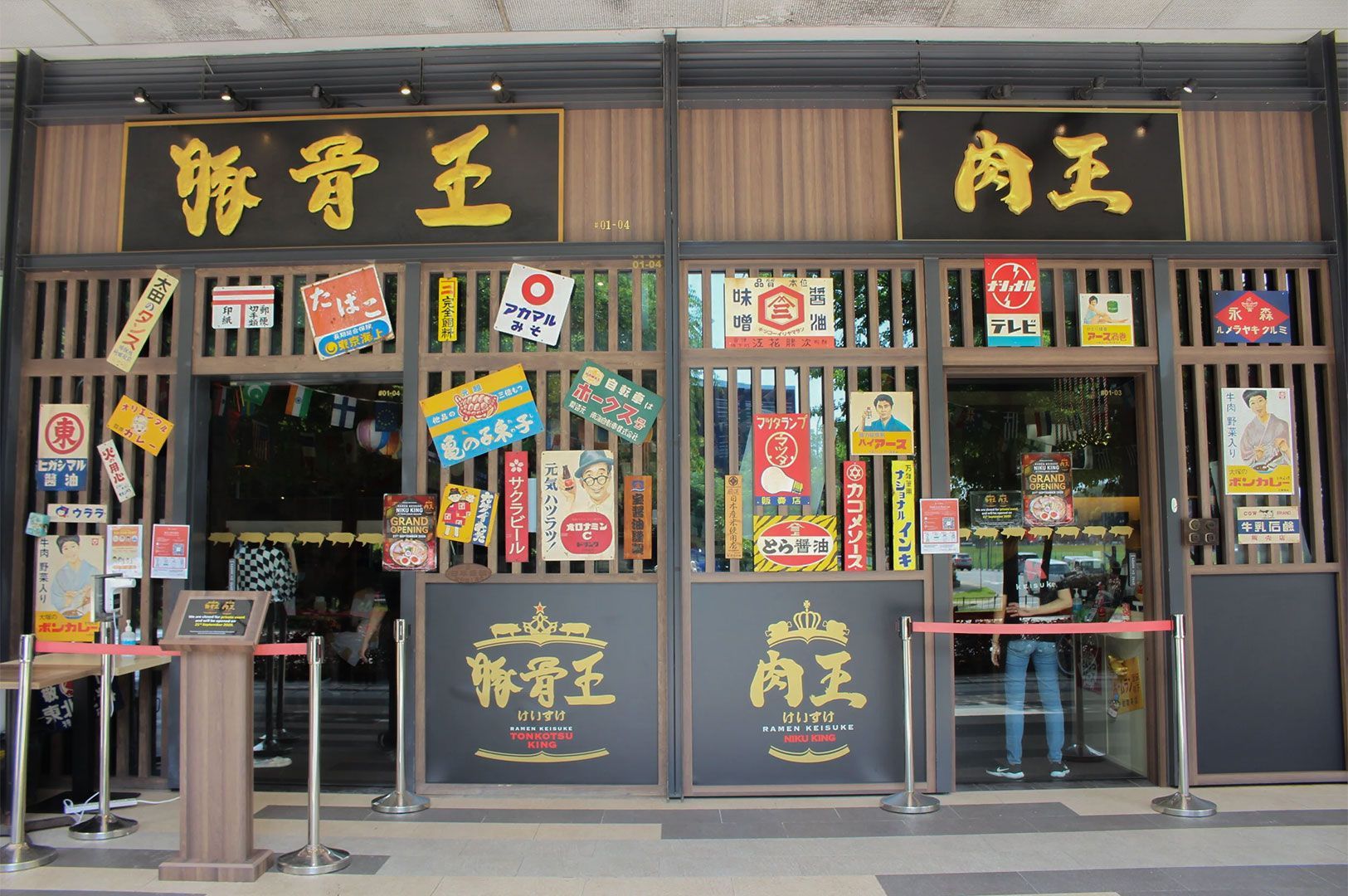 Exterior facade of a Japanese ramen restaurant (Ramen Keisuke) with prominent black and gold signage and traditional-style graphics and posters.