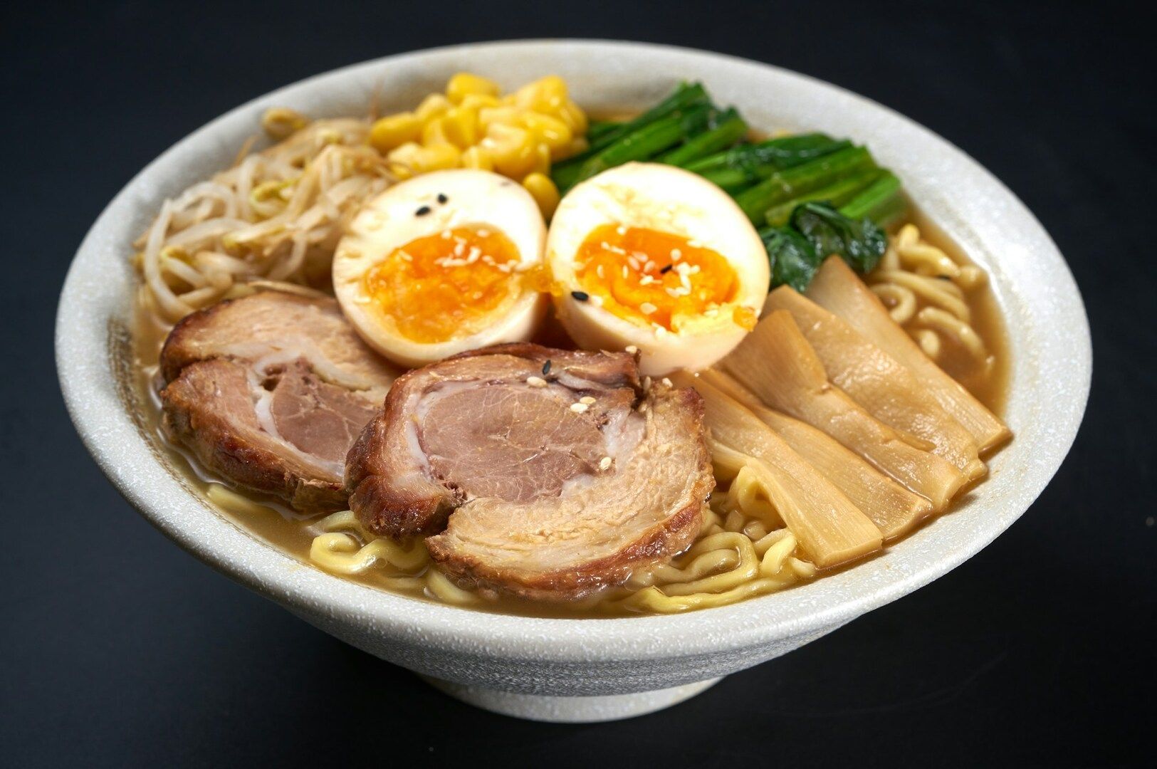 A bowl of ramen topped with sliced meat, soft-boiled eggs, and colorful vegetables.