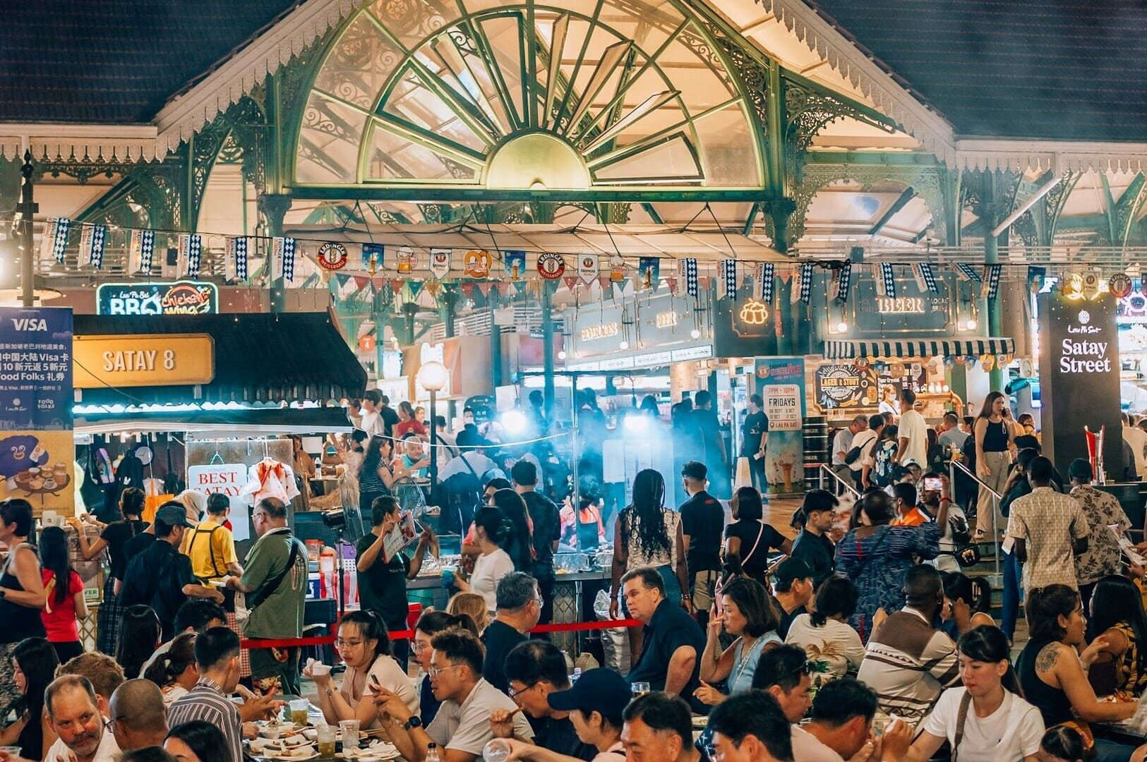 A bustling Singapore Hawker Centre filled with people enjoying food and drinks at various stalls.