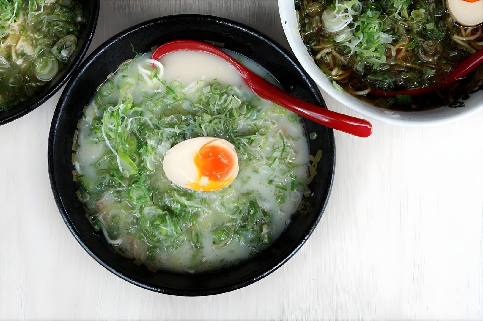 Three bowls of Singapore Vegetarian Ramen, each topped with a soft-boiled egg, arranged on a wooden table.