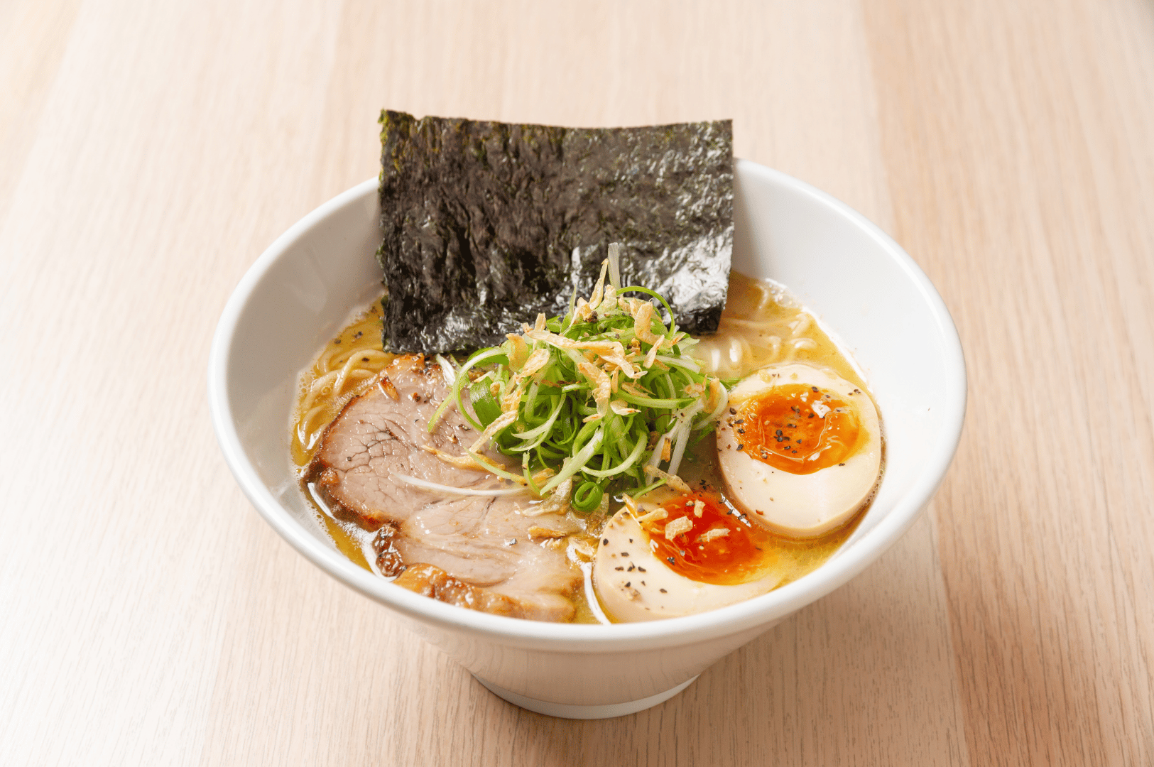 A creamy tonkotsu ramen bowl layered with chashu pork, soft-boiled egg, bean sprouts, green onions, and fermented nori. The fermented toppings add brightness and texture, balancing the deep umami of the pork bone broth and fatty cuts.