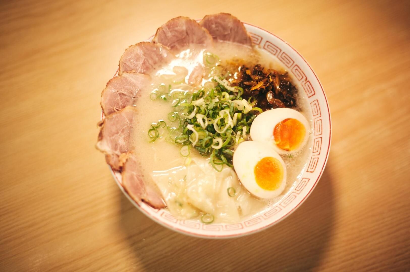 A steaming bowl of Hakata ramen featuring tender meat and a soft-boiled egg, served with green onions.