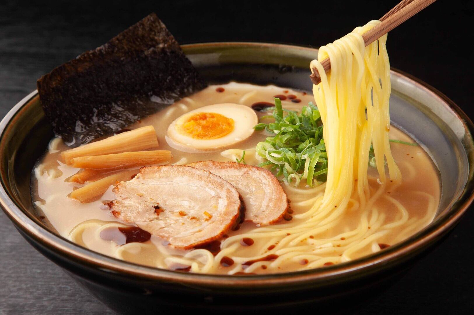 A bowl of Hakata ramen topped with slices of meat and colorful vegetables, served in a rich broth.