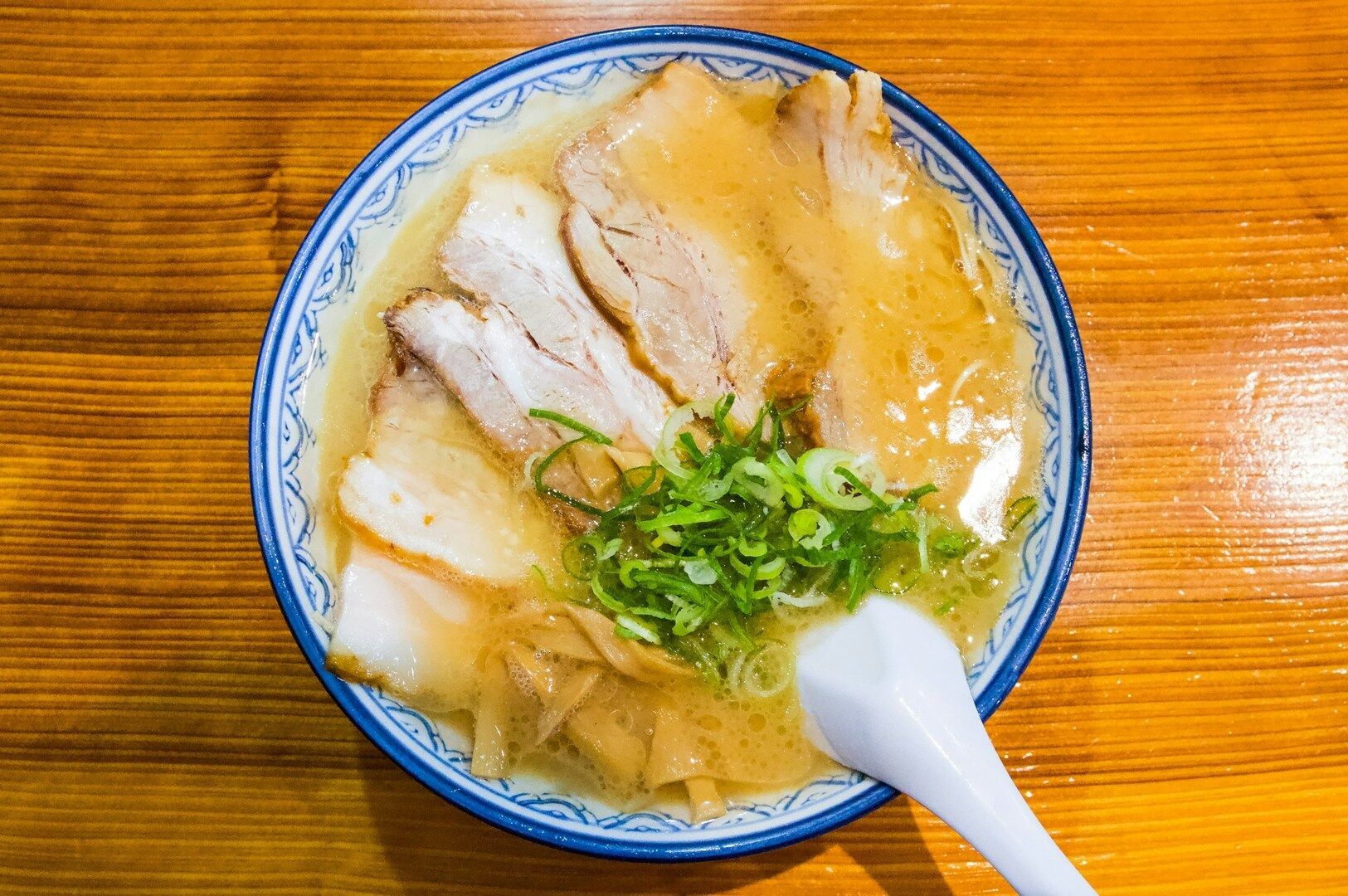 Tonkotsu Ramen in a bowl, showcasing savory broth, meat pieces, and vibrant green onions on top.