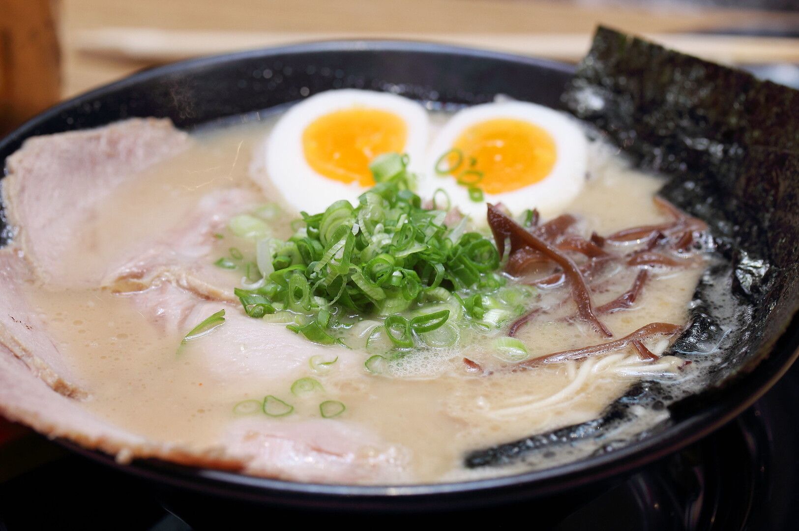 A bowl of Hakata ramen topped with a soft-boiled egg and slices of meat, garnished with green onions.