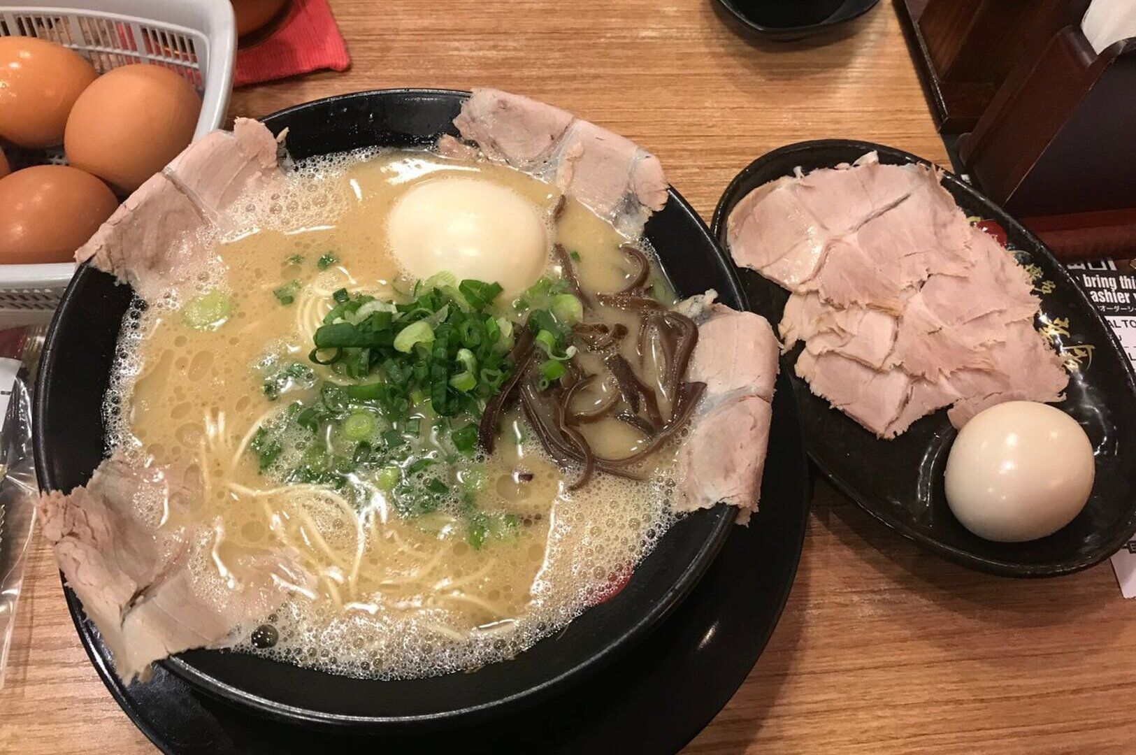 A serving of Hakata ramen featuring meat and eggs, displayed on a rustic table.