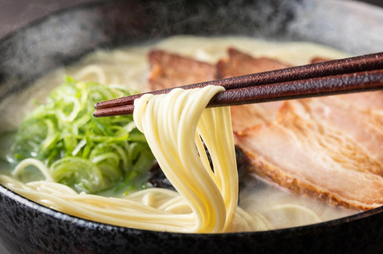 A bowl of Hakata Tonkotsu ramen topped with meat and fresh vegetables, showcasing a rich, savory.