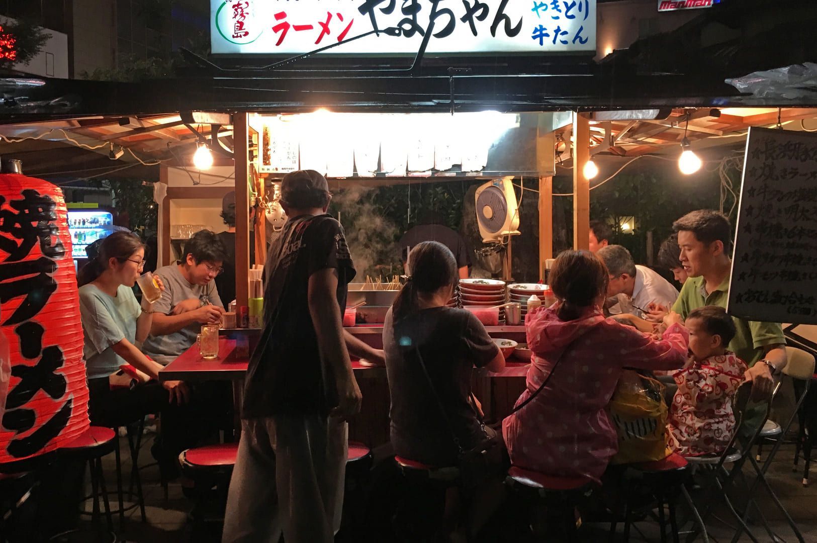 Diners gathered around a table at a Hakata Tonkotsu ramen shop, sharing a meal and conversation.