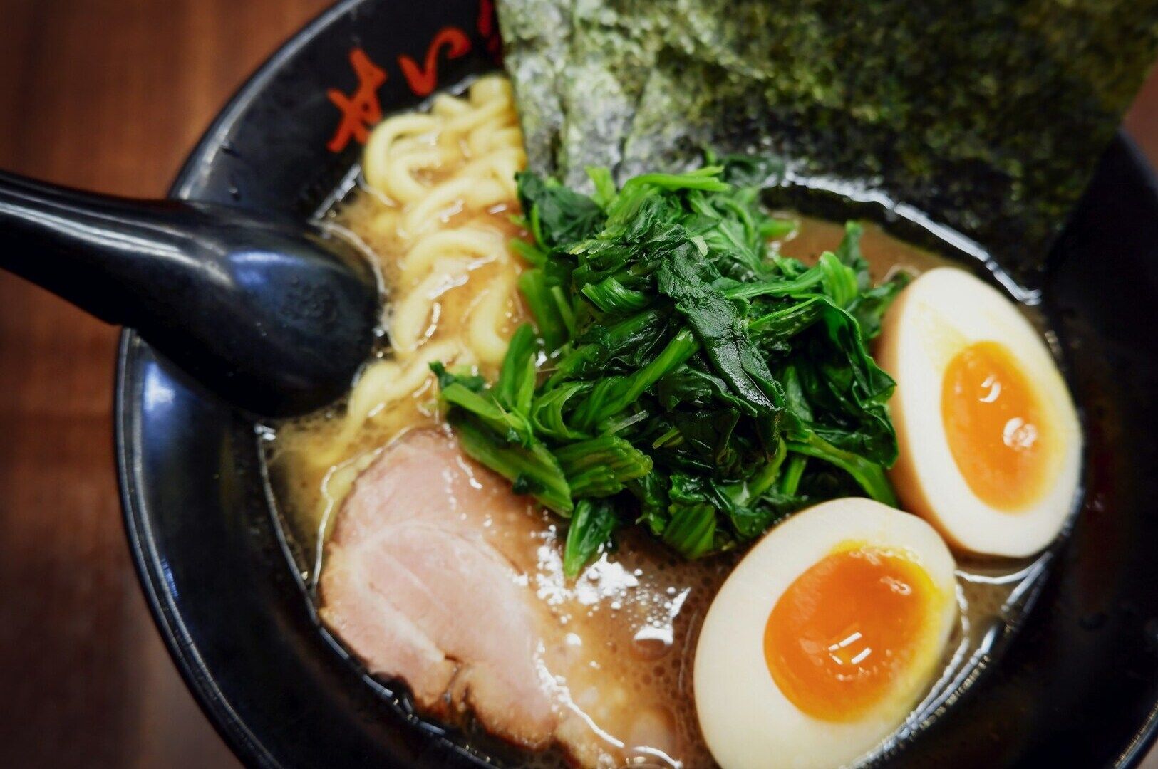 A steaming bowl of chicken-based ramen sits on a wooden counter, featuring tender slices of chicken.