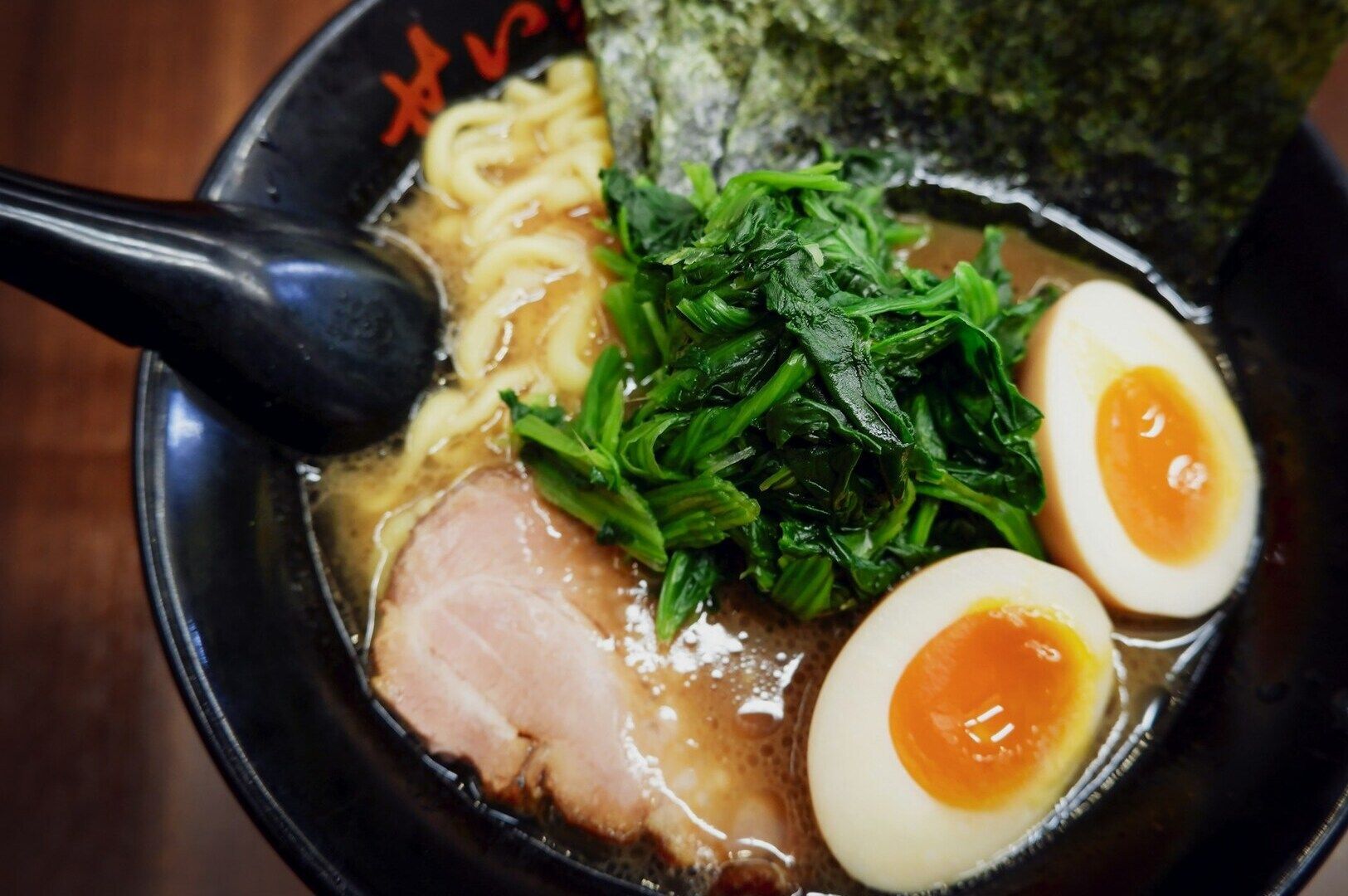 A bowl of Japanese ramen topped with meat, soft-boiled eggs, and fresh greens.