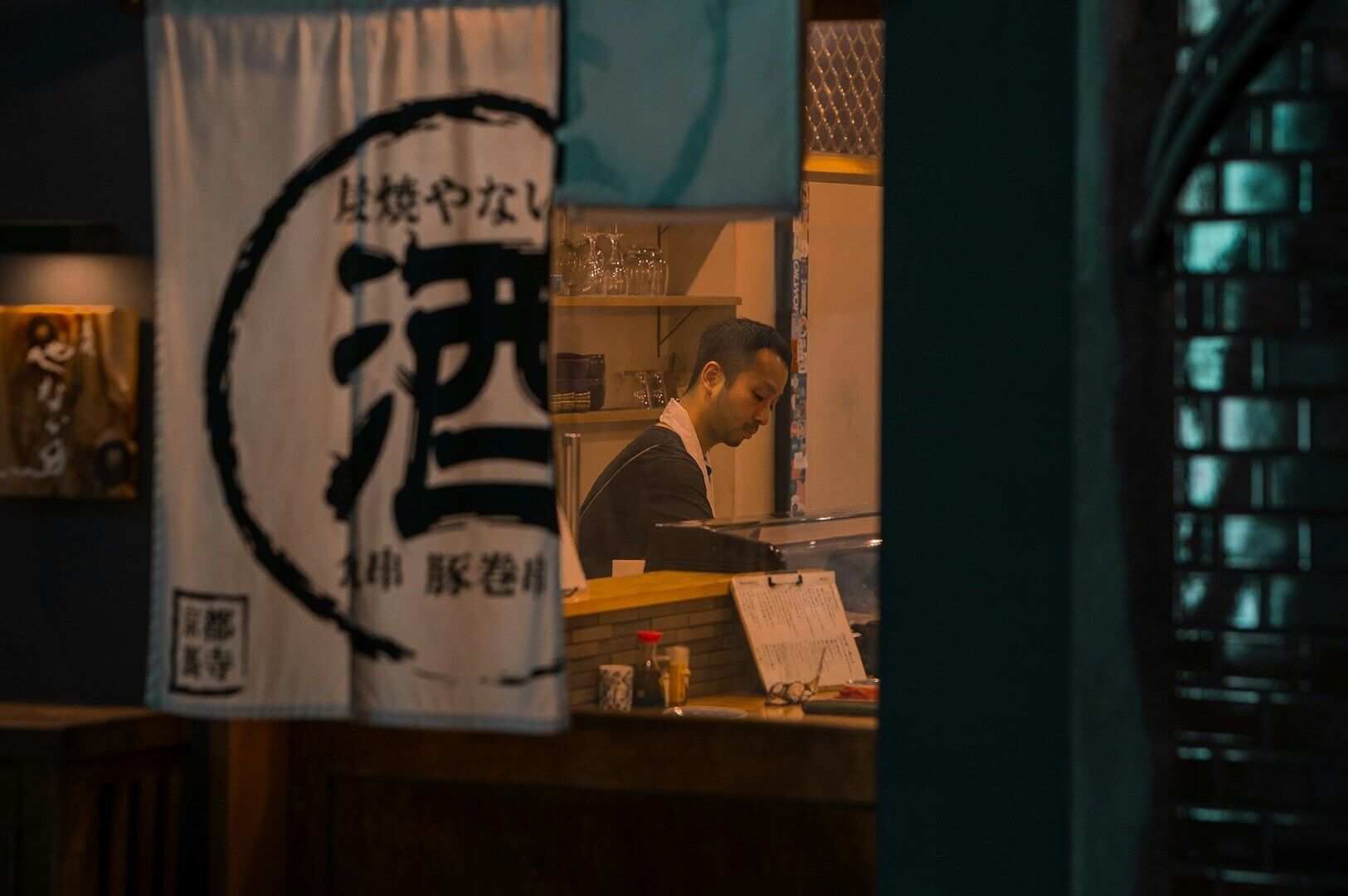 A man sits at a table in front of a ramen shop in Kyoto, Japan, indicating a restaurant or dining establishment.