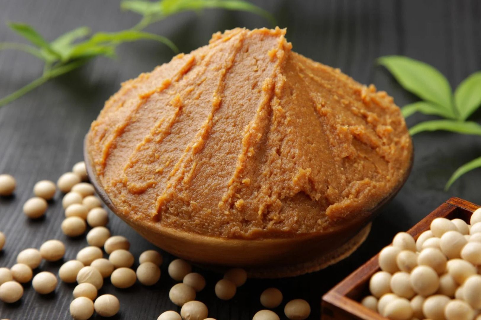 Miso paste in a bowl surrounded by soybeans on a rustic wooden table.