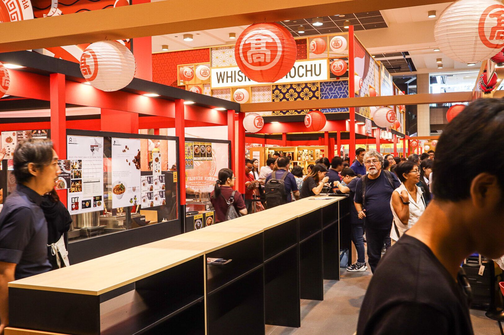 Patrons stands at the counter of a Japanese ramen shop in Singapore, surrounded by vibrant decor and menu displays.