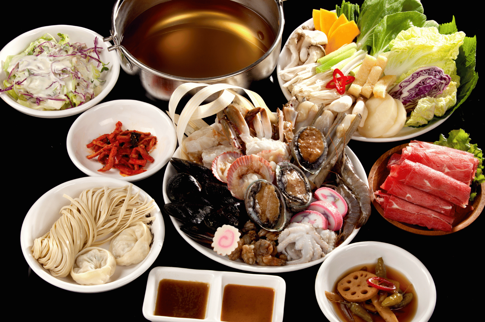 Traditional Asian hot pot spread with a central platter of seafood—shrimp, mussels, clams, abalone, squid, and fish cakes—surrounded by raw beef slices, fresh vegetables, noodles, dumplings, dipping sauces, and pickled sides, with a simmering broth pot ready for cooking, showcasing the richness of communal dining.