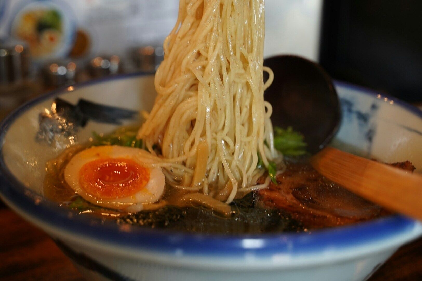 A steaming bowl of ramen with curly noodles, halved eggs, and tender meat, topped with fresh herbs.