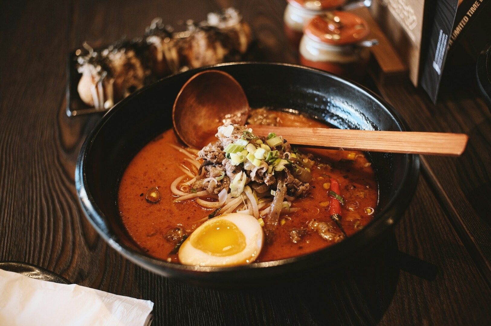 A bowl of ramen featuring rich broth, a soft-boiled egg, and a wooden spoon resting beside it.