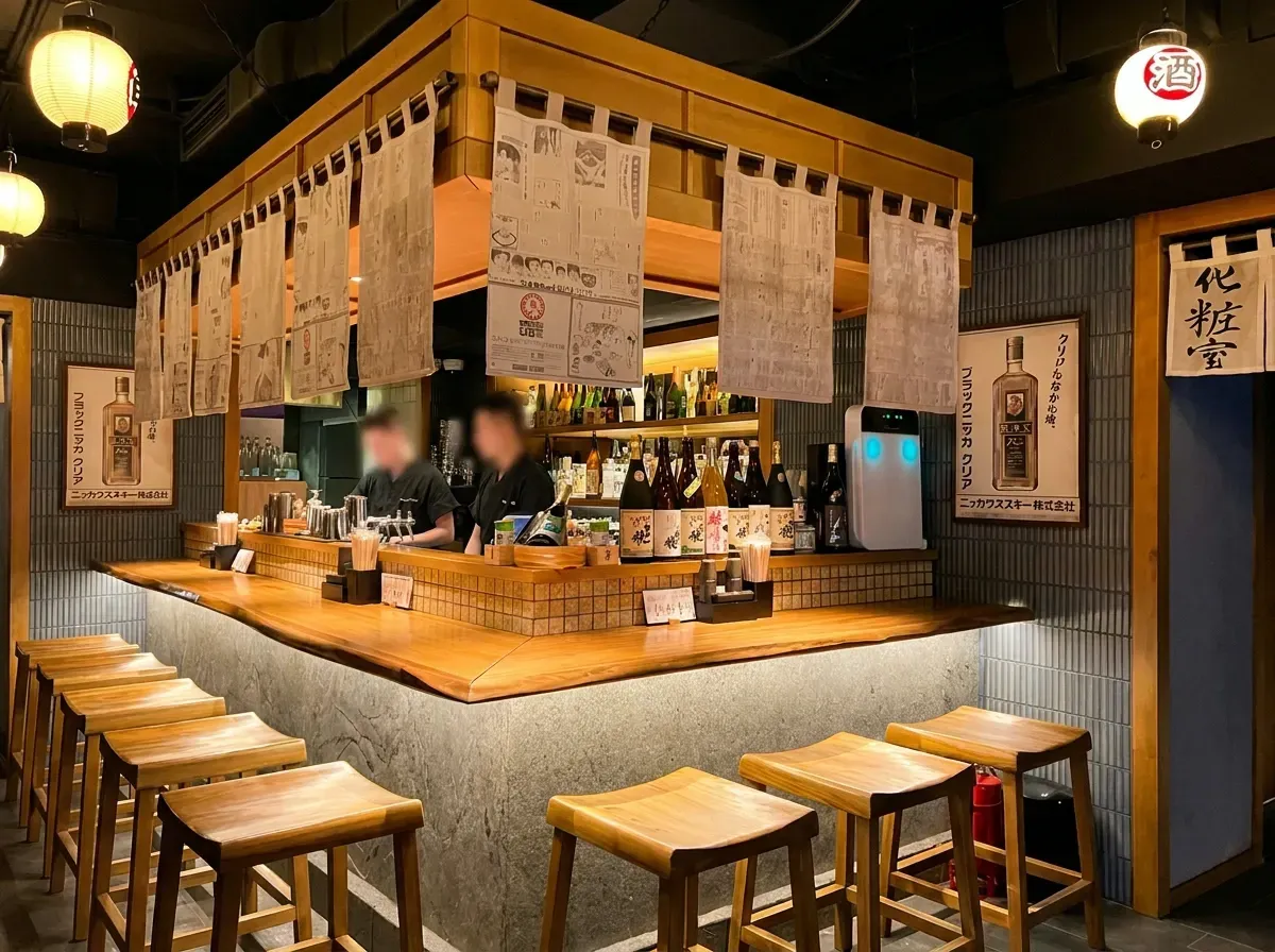 The interior of a traditional Japanese bar or ramen shop, featuring a wrap-around wooden counter.