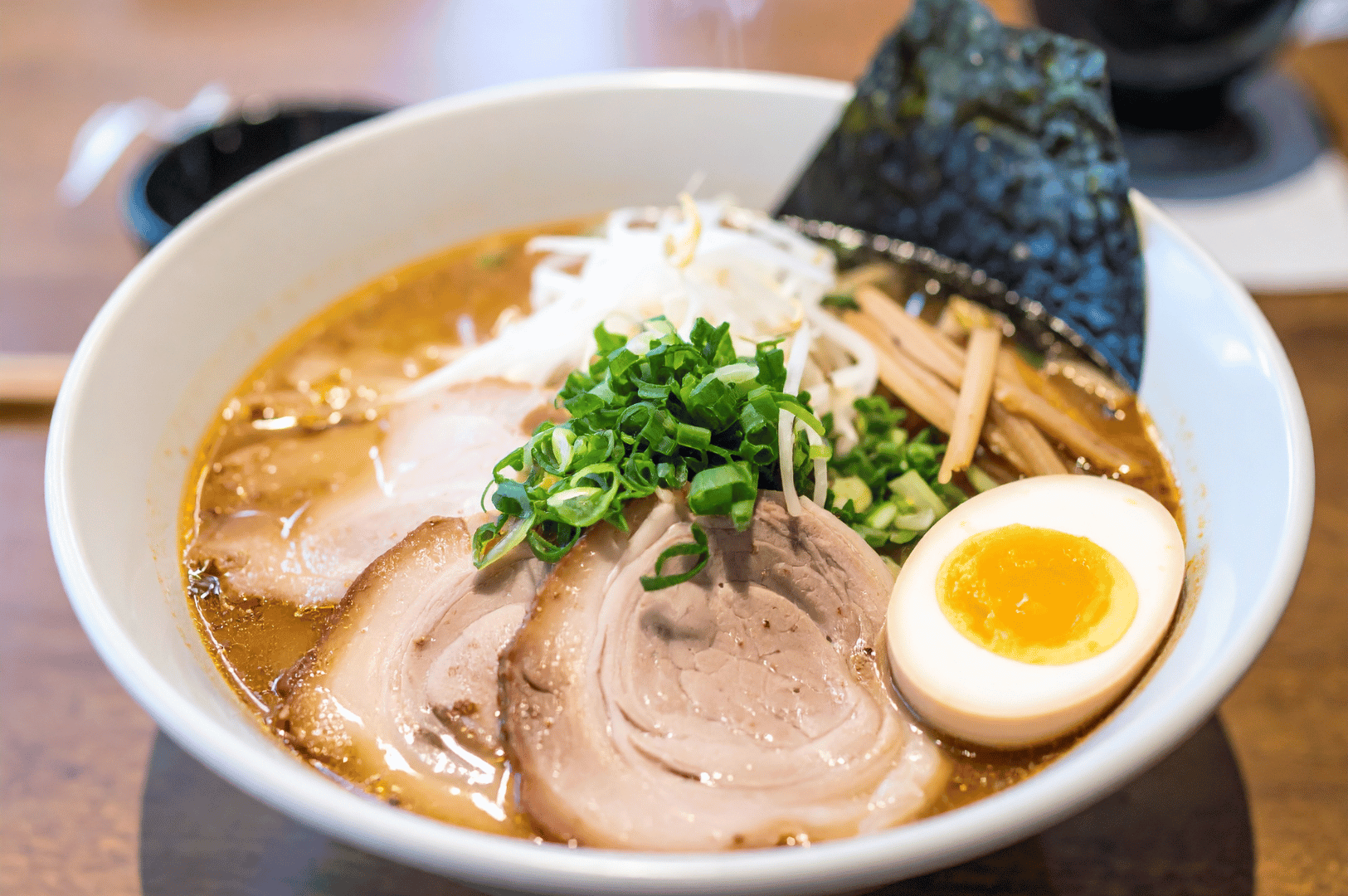 A white bowl of tonkotsu ramen showcases a rich, golden broth layered with chashu pork, soft-boiled egg, bean sprouts, bamboo shoots, green onions, and a crisp sheet of nori. The ingredients are artfully arranged, highlighting the harmony between texture, flavor, and visual appeal—an elegant finale to the scientific precision and cultural depth behind pork bone extraction.