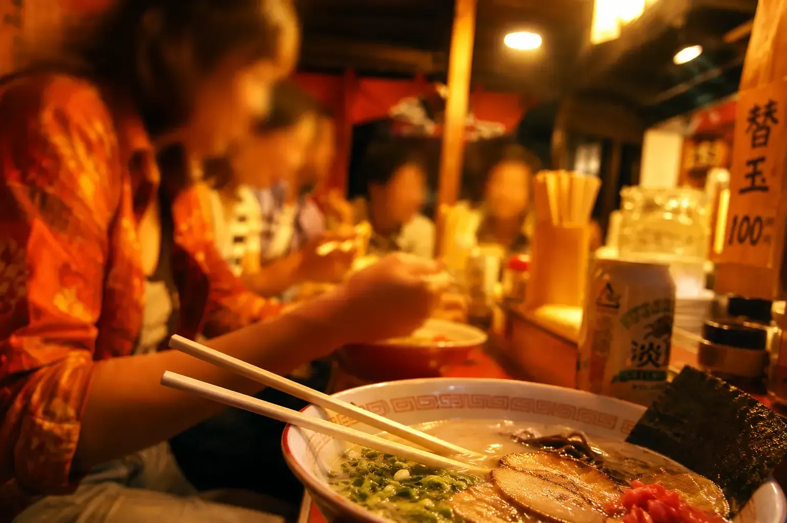 An open bowl of Tonkotsu ramen with chashu pork, green onions, and nori sits on a counter with chops