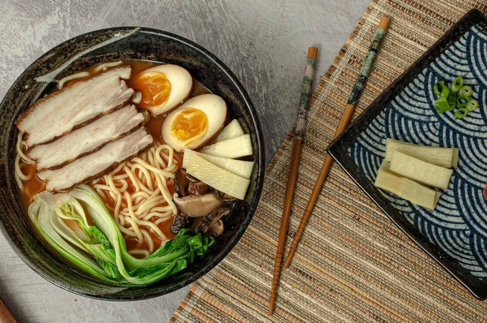 A bowl of Tonkotsu Black Ramen topped with meat, soft-boiled eggs, and fresh vegetables.