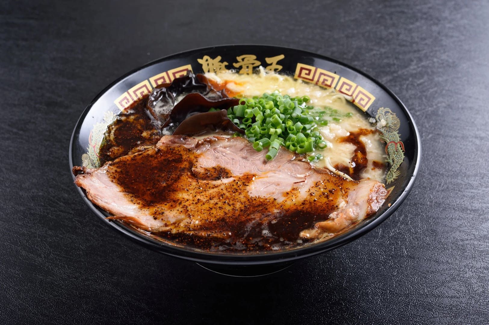 Tonkotsu Black Ramen in a bowl, featuring tender meat and assorted vegetables in a savory broth.